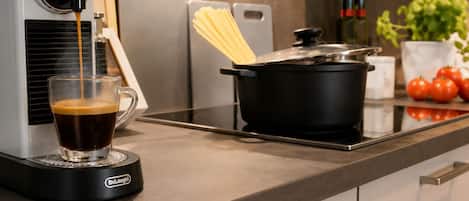 A kitchen with a coffee machine, a glass of coffee, a pot on the stove, and a cutting board with pasta.