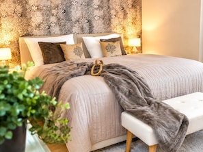 Un lit avec une tête de lit, plusieurs oreillers, une couverture et une table de chevet avec une lampe.