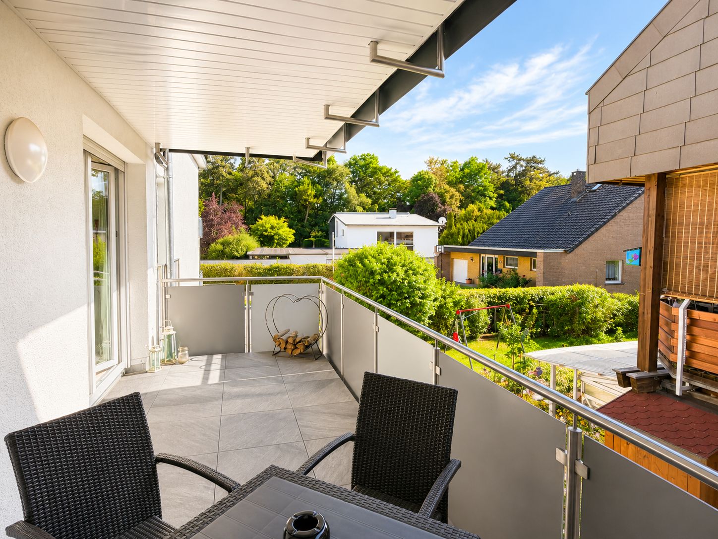 Un balcon avec une table et des chaises, une vue sur un quartier résidentiel et une allée couverte.