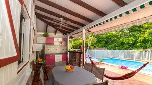 Un patio couvert avec une piscine, un coin repas avec une table et des chaises, et une cuisine avec des meubles de couleur rose.