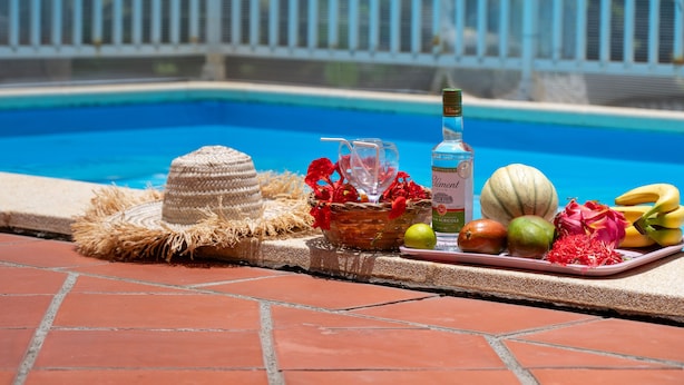 Une scène au bord de la piscine, avec un panier en osier, une bouteille et des fruits tropicaux.