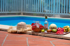 A poolside setting with a wicker basket, a bottle, and tropical fruits.
