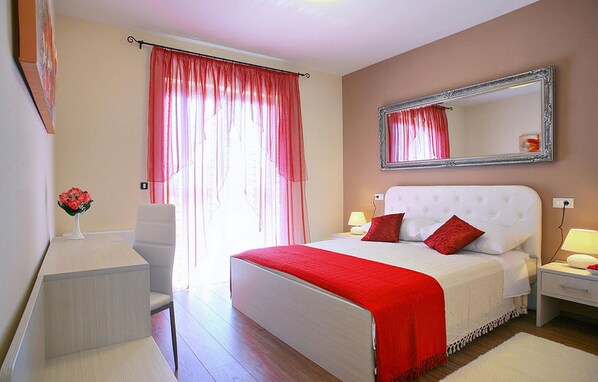 Een slaapkamer met een groot bed, een nachtkastje, een stoel, een spiegel en een raam met gordijnen.
