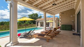 Ein überdachter Außenbereich mit Pool, Liegestühlen und Sonnenschirmen.