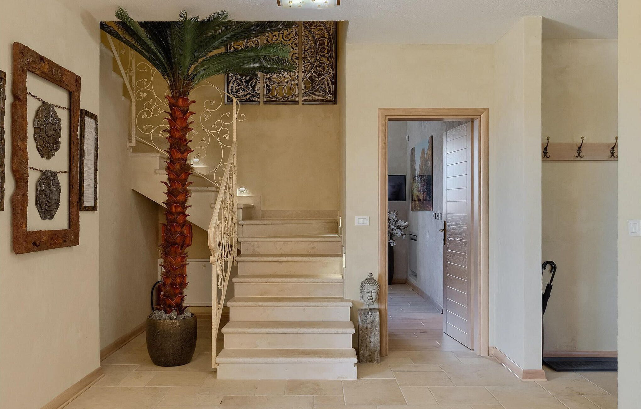 A staircase with a palm tree, framed artwork, and a Buddha statue.