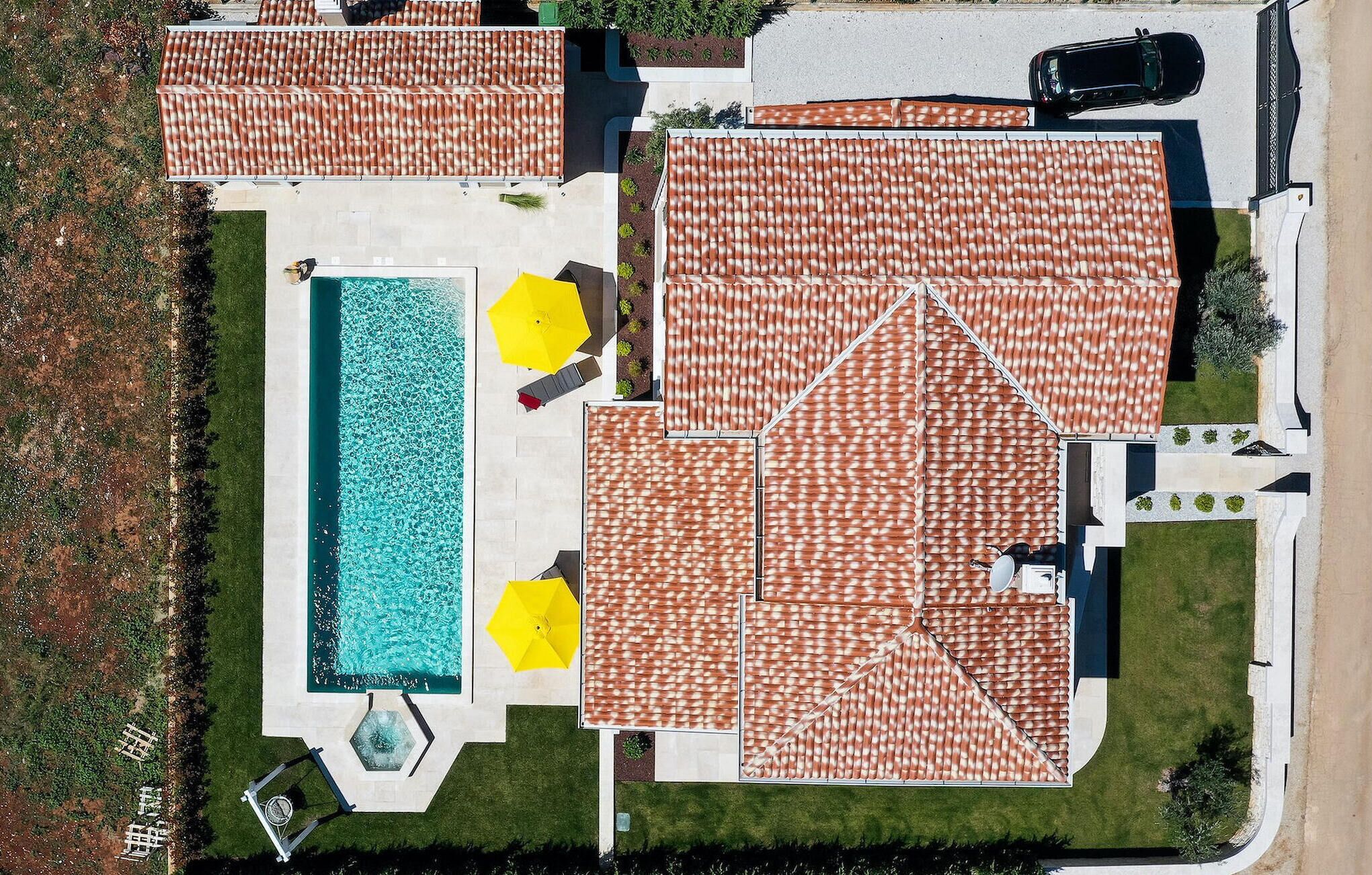 Vista aérea de una propiedad residencial con piscina, varios patios cubiertos y un coche aparcado cerca.