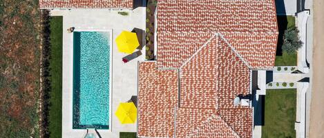 Vista aérea de una propiedad residencial con piscina, varios patios cubiertos y un coche aparcado cerca.