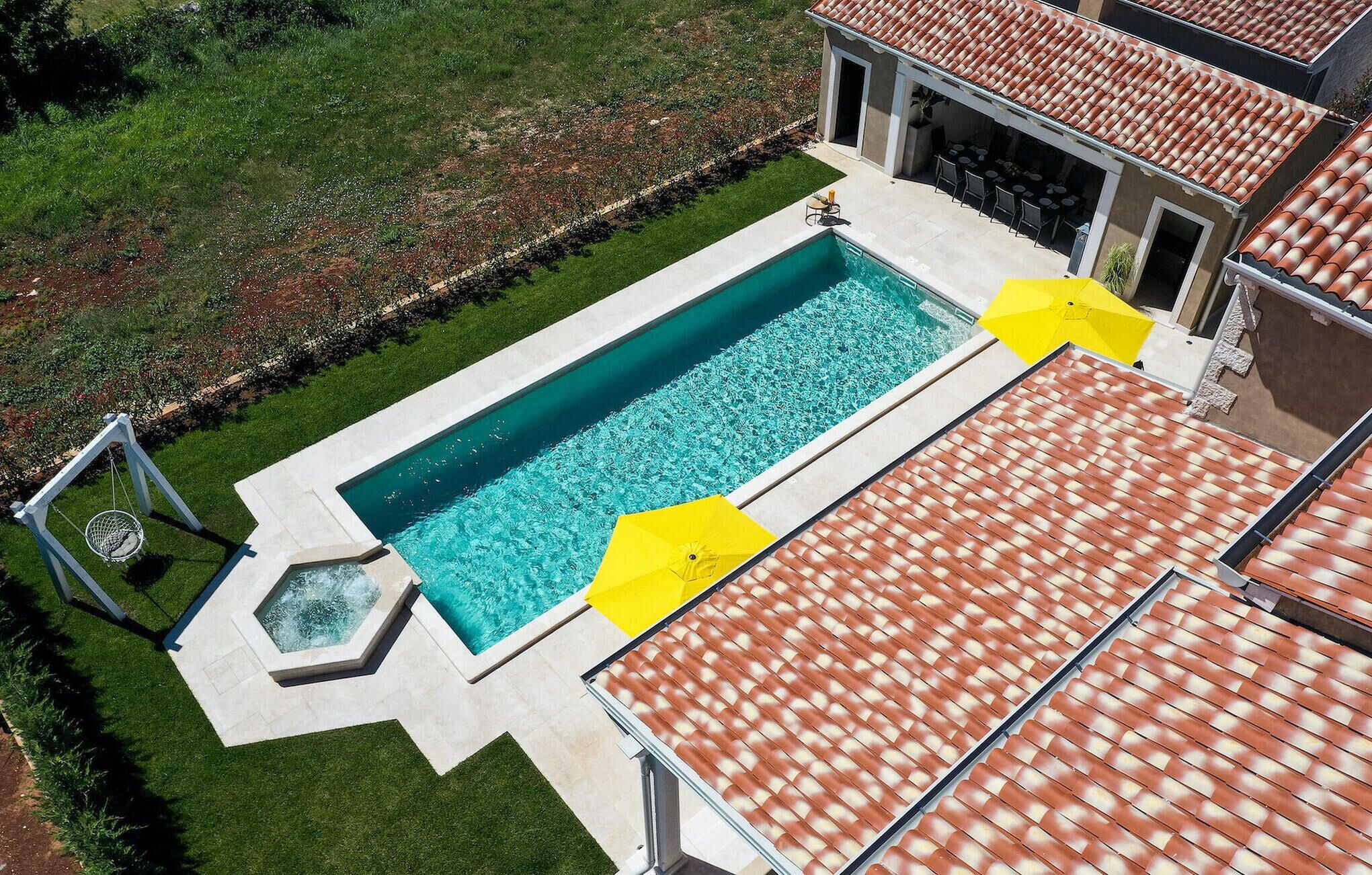 Una piscina rectangular con jacuzzi, rodeada por un césped cuidado y una zona de patio con mobiliario exterior.