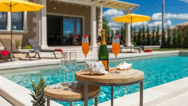 Ein Poolbereich mit Holztisch, zwei Champagnergläsern, einer Flasche und einer Ananas.