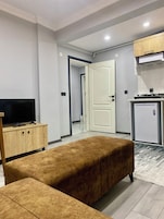 Un apartamento moderno con sala de estar amoblada, que incluye un sofá, televisor y cocina equipada con refrigerador y estufa.