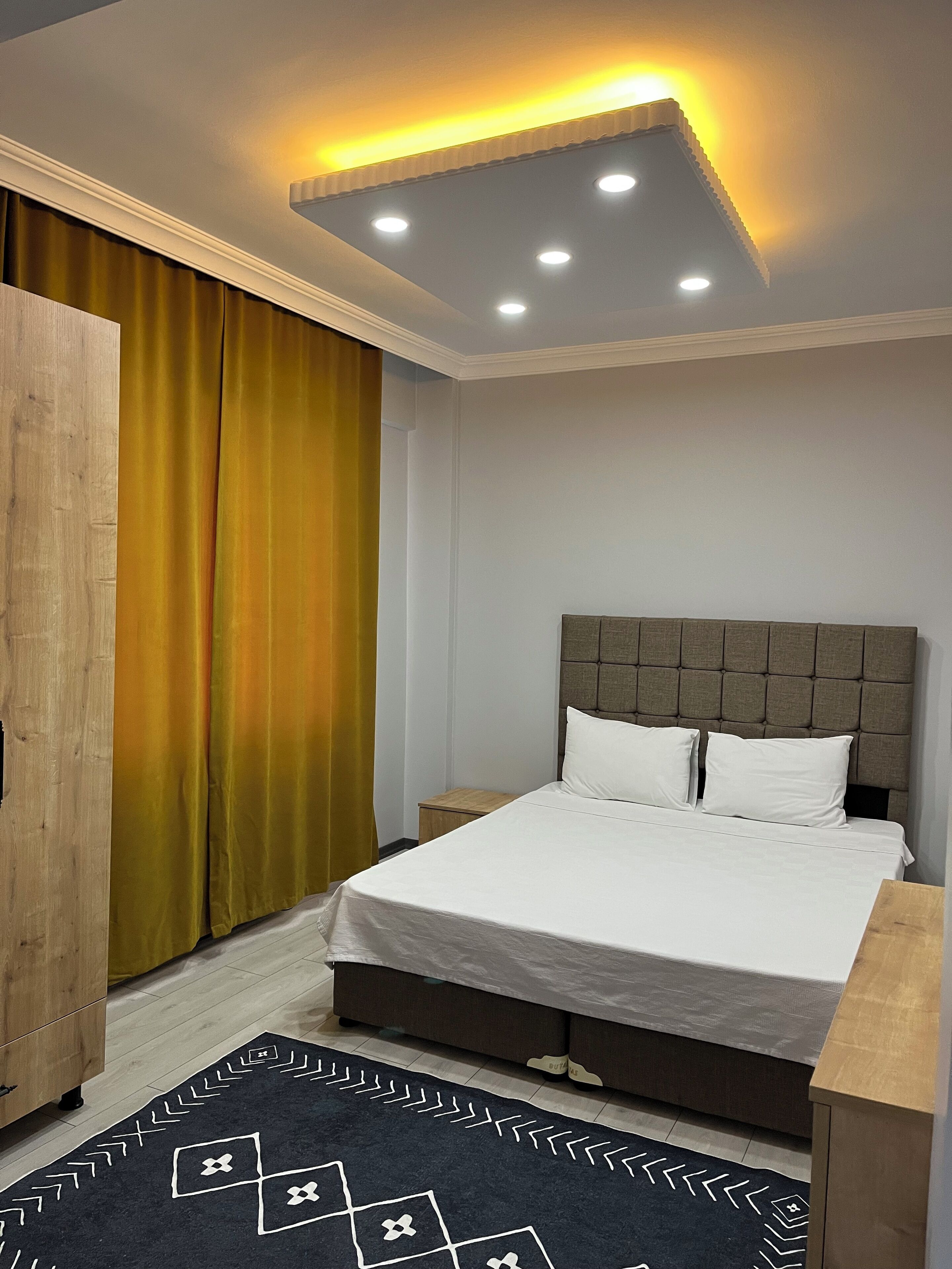 A modern bedroom with a bed, nightstands, a wardrobe, and a patterned rug.