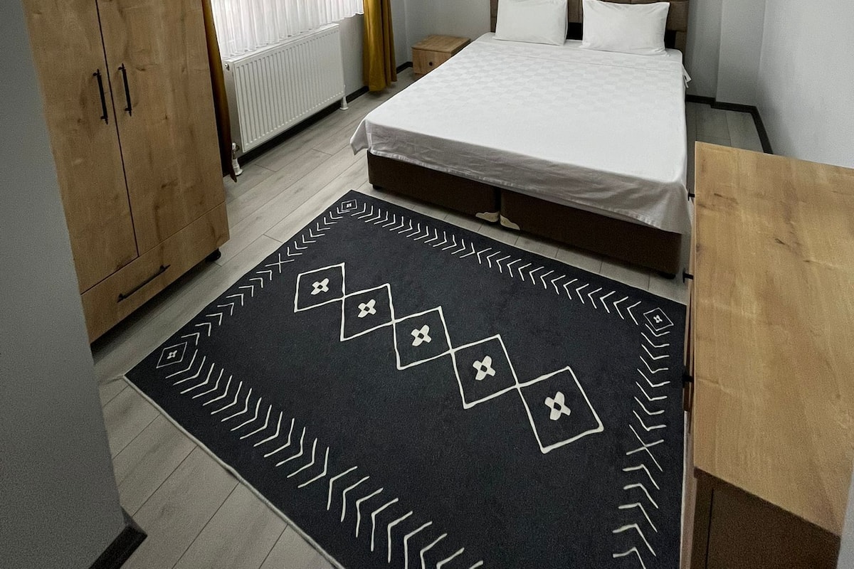 A modern bedroom with a large bed, wooden wardrobe, and a patterned rug.