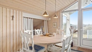 A dining area with a round wooden table, white chairs, and a view through large windows. - Nice home in Frøstrup with sauna (Frøstrup)