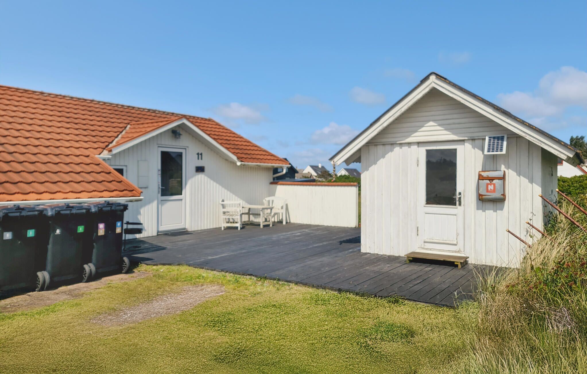 A small, single-story building with a red-tiled roof, a white door, and a small porch area.