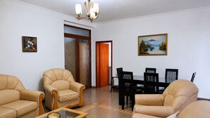 A living room with leather sofas, a glass coffee table, a dining table with chairs, a chandelier, and two paintings on the walls. - Saranda 55 (Sarandë)