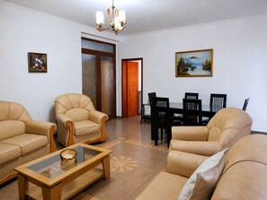 Un soggiorno con divani in pelle, un tavolino da caffè in vetro, un tavolo da pranzo con sedie, un lampadario e due quadri alle pareti.