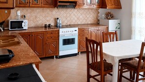 A kitchen with wooden cabinets, a stove, a microwave, and a dining area with chairs. - Saranda 55 (Sarandë)
