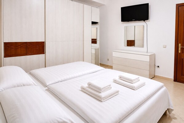 A hotel room with two beds, a TV, a mirror, and a wooden wardrobe.