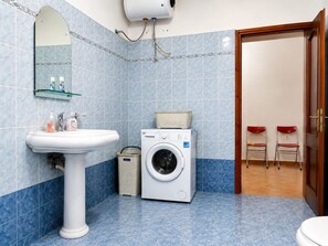 A bathroom with a sink, mirror, washing machine, and two red chairs.