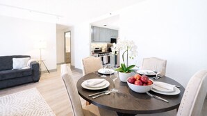 Un espace de repas moderne avec une table ronde dressée pour quatre personnes, un canapé et une cuisine en arrière-plan.