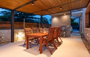 Eine Terrasse im Freien mit Holztisch und -stühlen, einem Grill und einer Steinmauer.