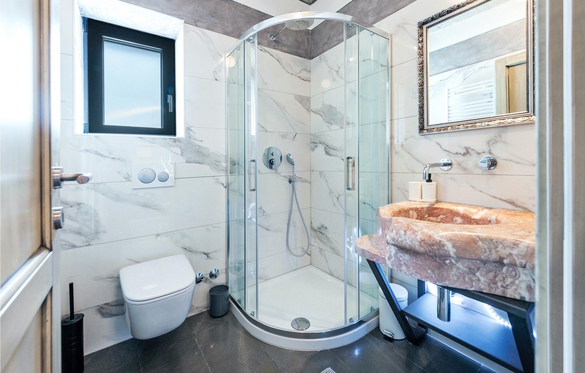 Een moderne badkamer met een douchecabine van glas, een marmeren wastafel en een toilet.