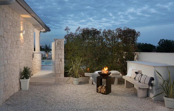Un patio con un brasero, asientos y una piscina al fondo.