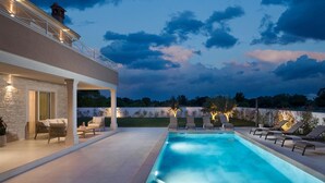 A modern outdoor pool area with a two-story building, lounge chairs, and a stone wall. - Villa Simona Residence (Zminj)