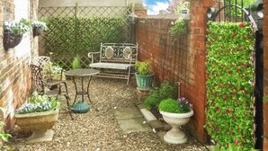 Eine Gartenpatiо mit einer Metallbank, einem kleinen runden Tisch und Topfpflanzen.