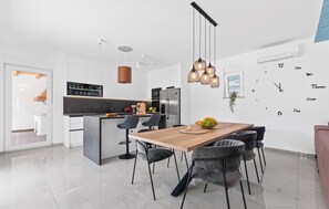 Una cocina moderna con armarios blancos, una isla central y un comedor con una mesa de madera y sillas grises tapizadas.