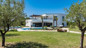 Una casa moderna de dos pisos con piscina, rodeada de césped cuidado y árboles.