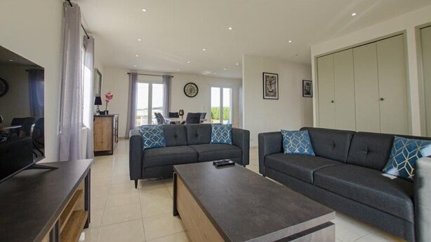 A modern living room with two sofas, a coffee table, and a dining area with a table and chairs. - Le Paradis de L'orient (PUITS ET NUISEMENT)