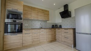 A modern kitchen with wooden cabinets, stainless steel appliances, and patterned backsplash tiles. - Le Paradis de L'orient (PUITS ET NUISEMENT)