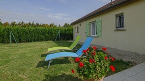 A house with a garden, two lawn chairs, a swing set, and a flower bed with red flowers. - Le Paradis de L'orient (PUITS ET NUISEMENT)