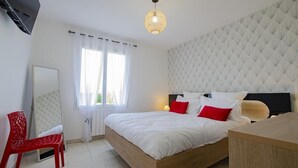 A bedroom with a bed, a red chair, a bedside table, a mirror, and a ceiling light. - Le Paradis de L'orient (PUITS ET NUISEMENT)