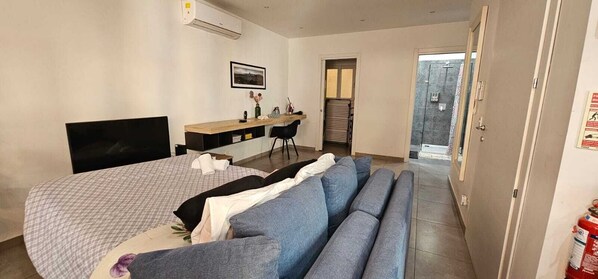 A bedroom with a bed, a desk, a chair, a sofa, and a door leading to a balcony.