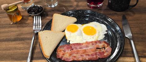 Un plato de desayuno con huevos, tocino, tostadas y un tazón pequeño de granola.