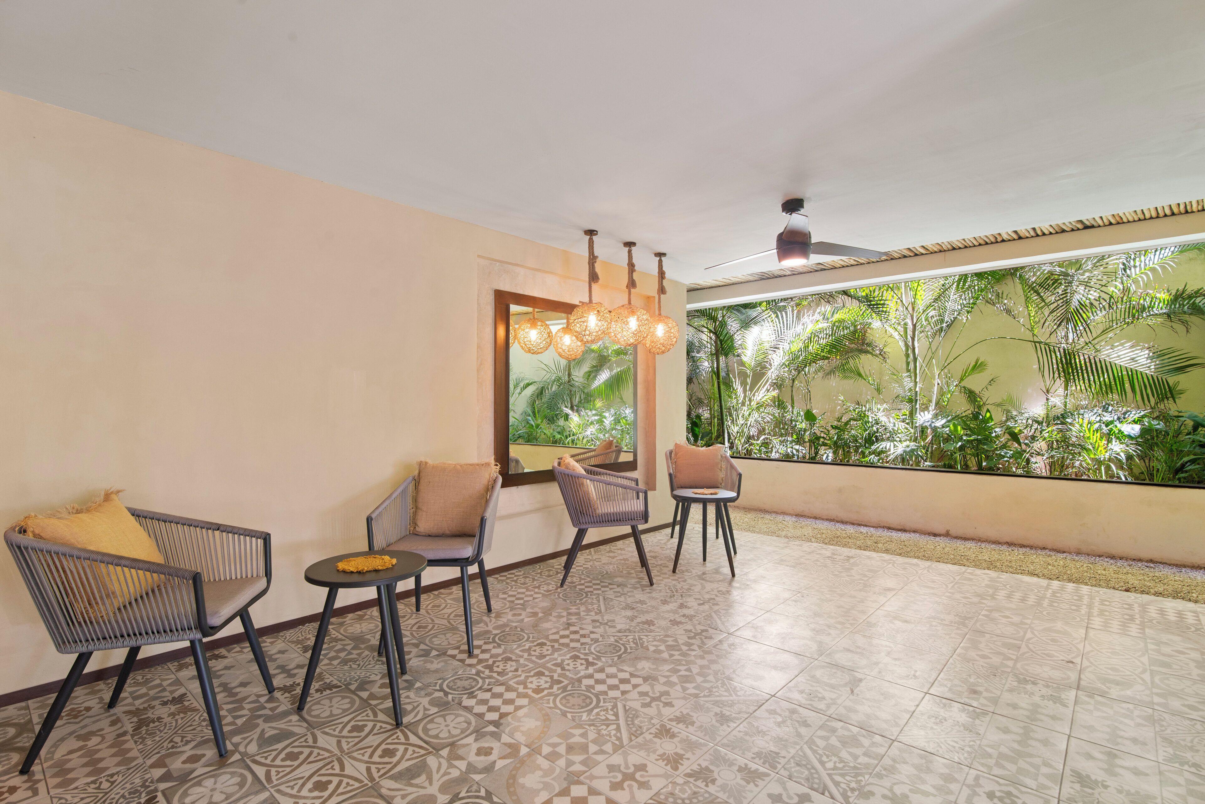 A room with patterned floor tiles, a ceiling fan, and a view of lush greenery through a window.