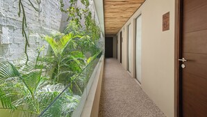 Un pasillo con pared de vidrio que exhibe plantas de interior, techo de madera y una puerta con el signo del número.