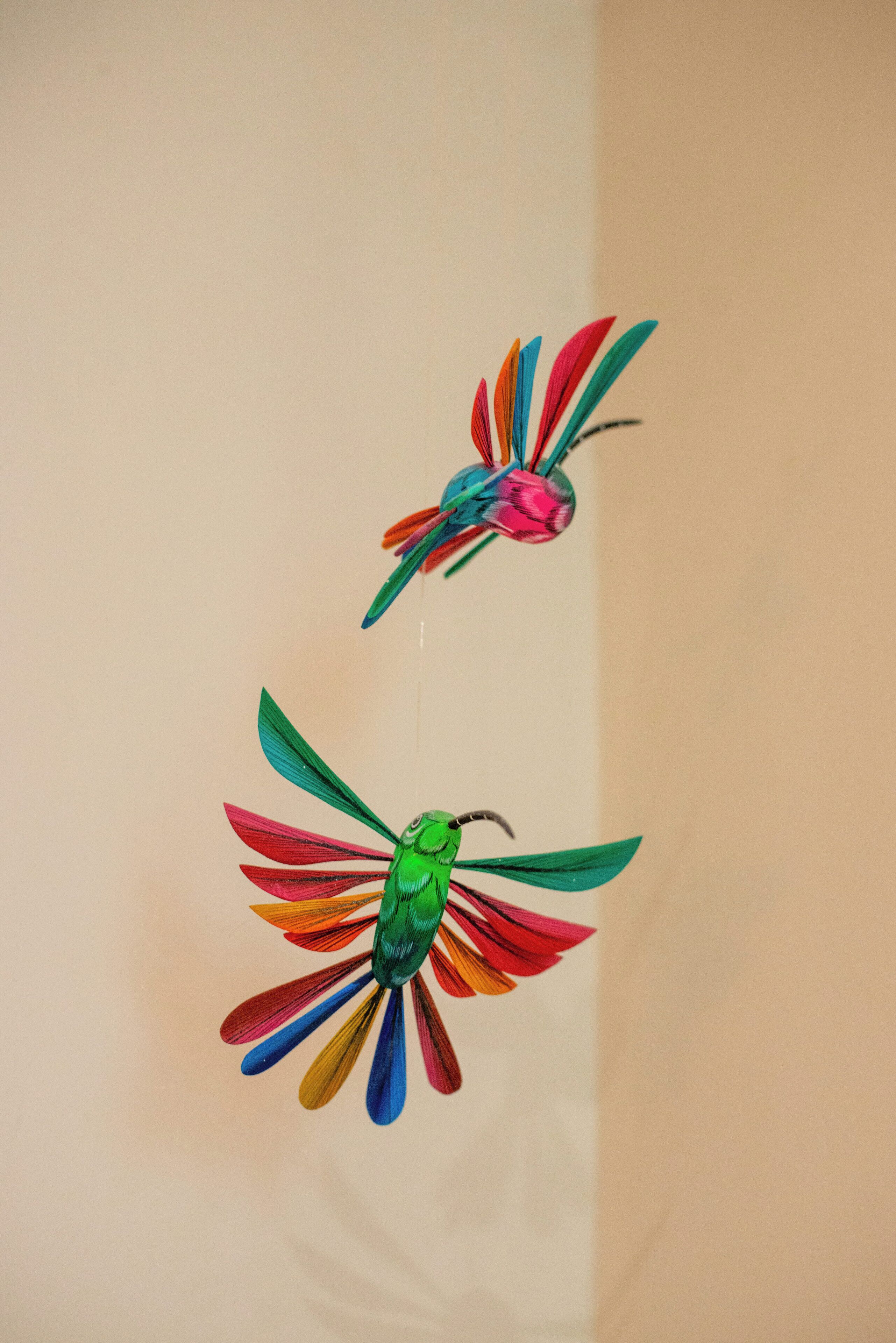 Two colorful paper birds hanging on a wall.