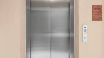 A modern elevator with a control panel on the wall, a wooden sign above it, and a textured ceiling.