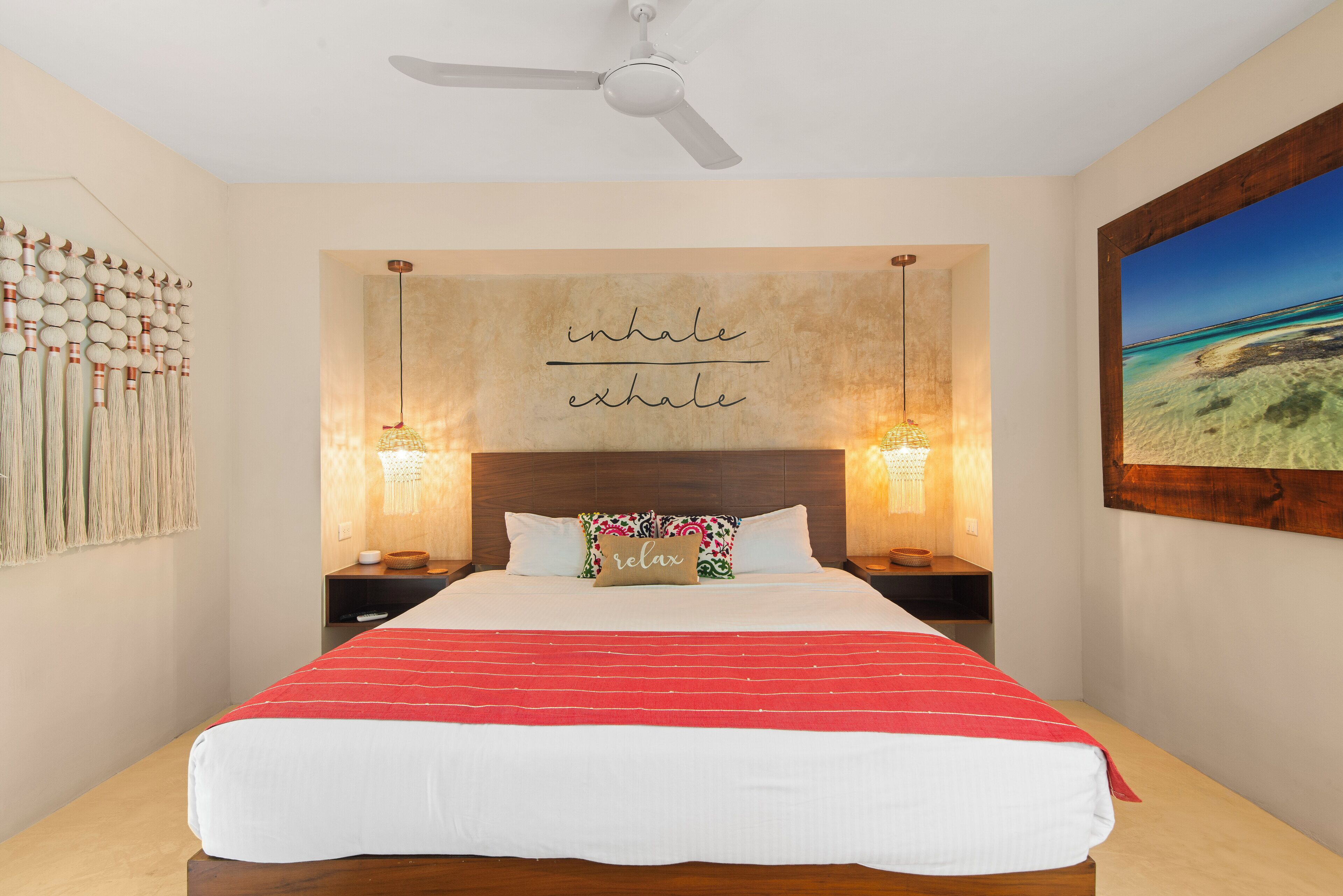 Une chambre à coucher avec un lit, un ventilateur de plafond, un mur orné d’une citation inspirante et un tableau encadré.