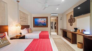 A hotel room with two beds, a TV, a ceiling fan, a painting, and a desk with a lamp.