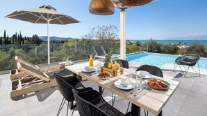 A dining area with a table set for two, overlooking a pool and a scenic view.