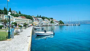 A waterfront promenade with a row of buildings, a stone pathway, and boats docked along the shore.