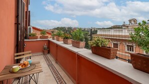 A balcony with potted plants, a table with croissants, and a view of buildings and clouds. - Top view luxury apartment Piazza del Popolo (Roma)