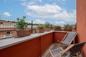 Un balcon agrémenté de plantes en pot, avec une chaise et une vue sur les immeubles.