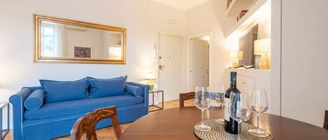 A living room with a blue sofa, a wooden dining table with wine glasses, and a mirror on the wall.