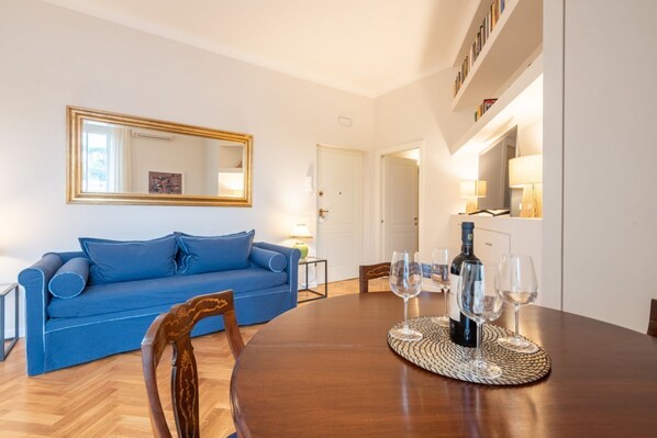 Un salon avec un canapé bleu, une table à manger en bois avec des verres à vin, et un miroir au mur.