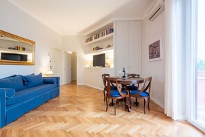 Un salon avec un canapé bleu, une table à manger en bois avec des chaises, un téléviseur et des étagères.